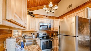 A kitchen with wooden cabinets, a stainless steel refrigerator, an oven, a microwave, and a chandelier. - 🏔Sunset Mtn views!⛰ 5 min to PFORGE🚙  HOT TUB! ♨️ (Pigeon Forge)