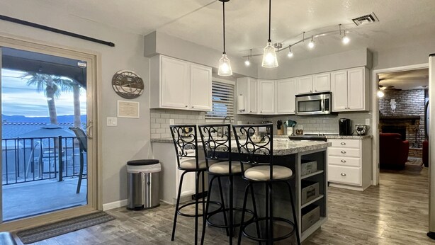 A modern kitchen with white cabinets, a stainless steel sink, and a bar area with stools.
