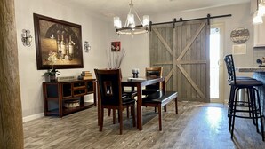 A dining area with a wooden table, chairs, and a chandelier. There is a sliding barn door in the background.