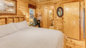 A wooden cabin bedroom with a bed, a small table with a Christmas tree, and a mirror on the wall. - Sunrise View-10 Min to Blue Ridge,Hot Tub-3 BR (Blue Ridge)