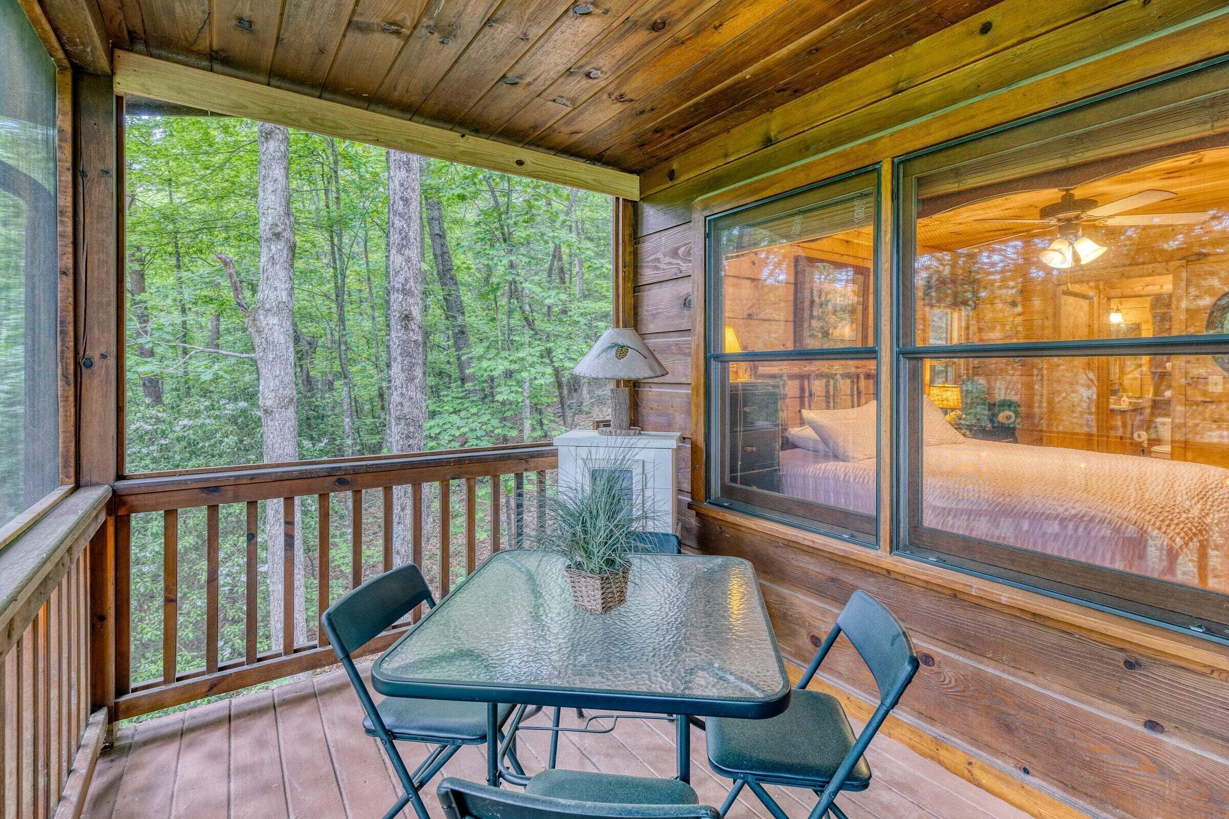 Una cabaña de madera con un porche acristalado, una mesa con sillas y vista a un bosque.