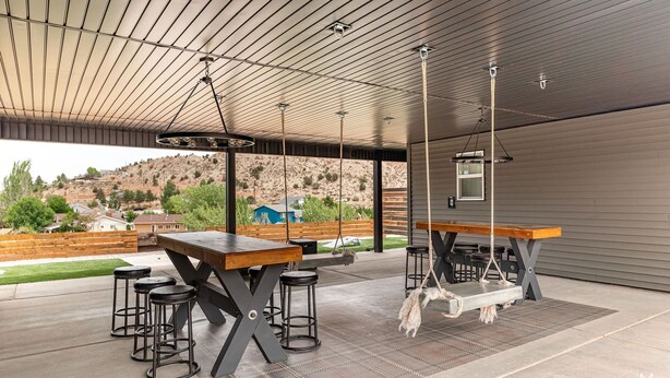 Une terrasse extérieure avec une table en bois et des tabourets de bar, une balançoire suspendue et une vue sur un paysage vallonné.