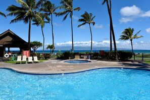 Une piscine avec des chaises longues, des palmiers et une vue sur l’océan.