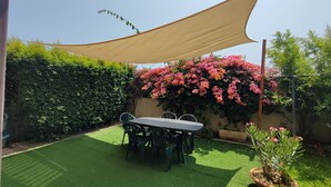 Un patio con una mesa, sillas, una planta en maceta y un arbusto grande con flores.