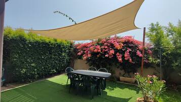 Un patio con tavolo e sedie, una pianta in vaso e un grande arbusto fiorito.