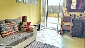 Una sala de estar con sofá, alfombra estampada y vistas al exterior a través de un ventanal.