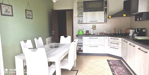 Cozinha com armários brancos, mesa de jantar com cadeiras e micro-ondas sobre a bancada.