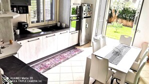 Una cocina con comedor, refrigerador, microondas y ventana con persianas.