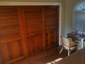 Relax in this serene space with a large wardrobe, a wicker chair, and a desk with a lamp.