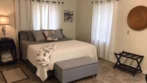 Un dormitorio con cama, mesita de noche, banco y cortinas.