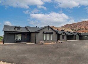 Une maison moderne à deux étages, dotée d’une grande allée et surplombant un paysage montagneux.