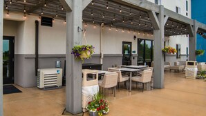 An outdoor patio area with tables and chairs, a covered seating area, hanging flower baskets, and an air conditioning unit.