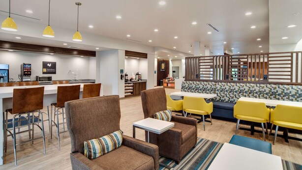 A modern hotel lobby with a bar area, seating arrangements, and a kitchen in the background.
