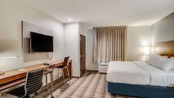 Une chambre d’hôtel comprenant un lit, un bureau avec une chaise, une télévision et une fenêtre avec des rideaux.