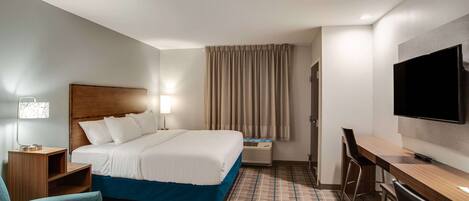 A hotel room with a bed, a desk, a chair, a TV, and a lamp.