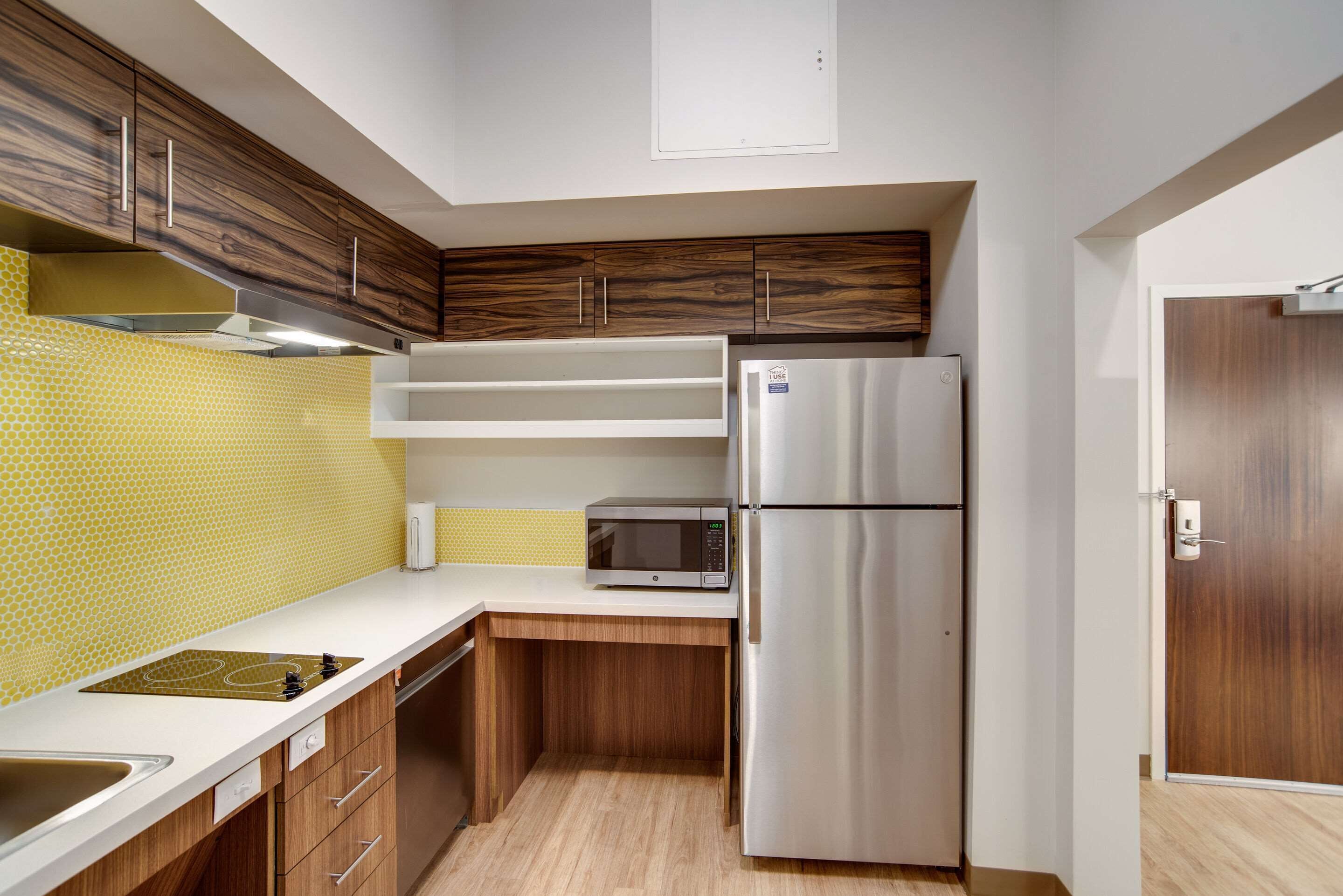 A compact kitchen with a microwave, refrigerator, wooden cabinets, and a yellow patterned backsplash.