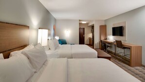A hotel room with two beds, a desk, a chair, a television, and a bathroom visible through an open door.