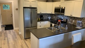 A modern kitchen with white cabinets, stainless steel appliances, a black countertop, and a tiled backsplash.