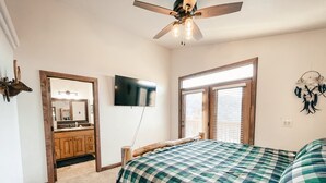 A bedroom with a bed, a ceiling fan, a TV, and a window with blinds.