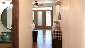 A hallway with a chandelier made of antlers, a welcome sign, a checkered table, and a view through a door to a balcony.
