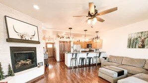 A spacious living room with a fireplace, a kitchen with wooden cabinets, and a ceiling fan.