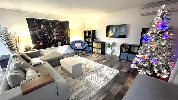 Ein modernes Wohnzimmer mit einem grauen Sofa, einem blauen Sessel, einem weißen Weihnachtsbaum und einem Flachbildfernseher.