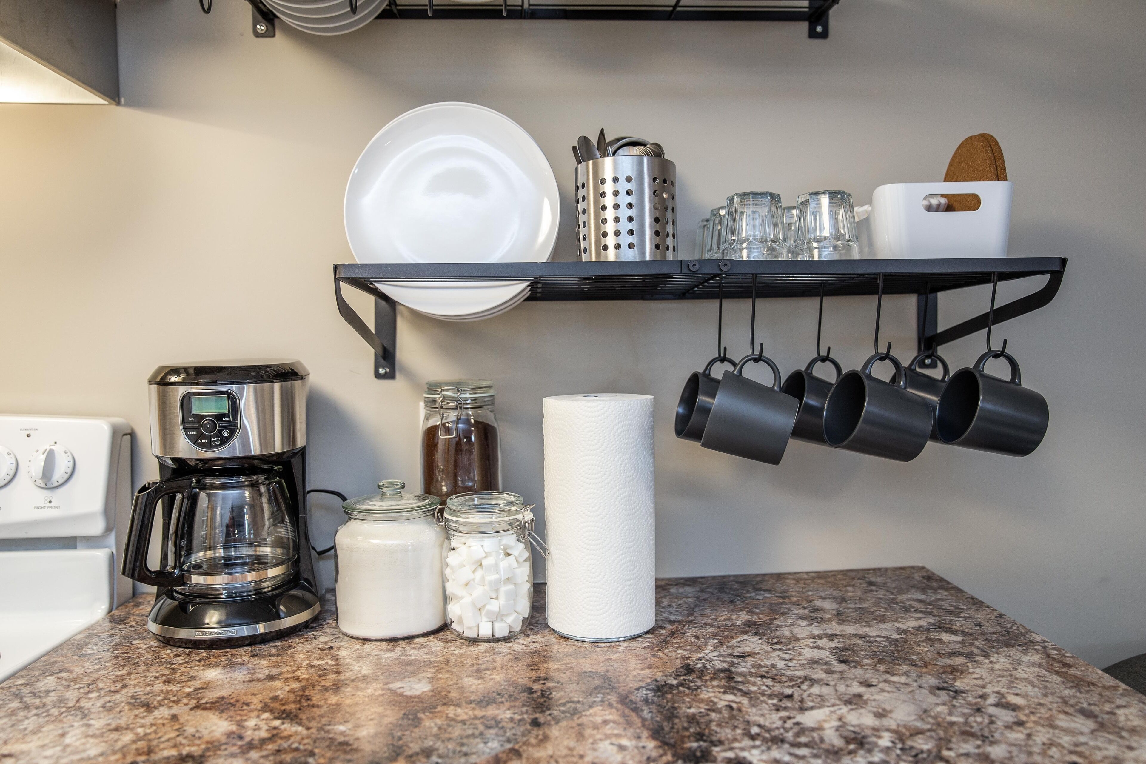 A kitchen with a coffee maker, jars, a paper towel holder, and hanging pots.