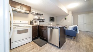 A compact kitchen with a stove, dishwasher, and a small seating area with a chair. - ★Bright Modern Suite ★ Netflix - WiFi ✔Long Stays ★ Clean (Edmonton)