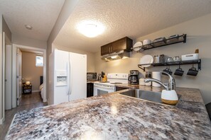 A modern kitchen with granite countertops, stainless steel appliances, and open shelving. - ★Bright Modern Suite ★ Netflix - WiFi ✔Long Stays ★ Clean (Edmonton)