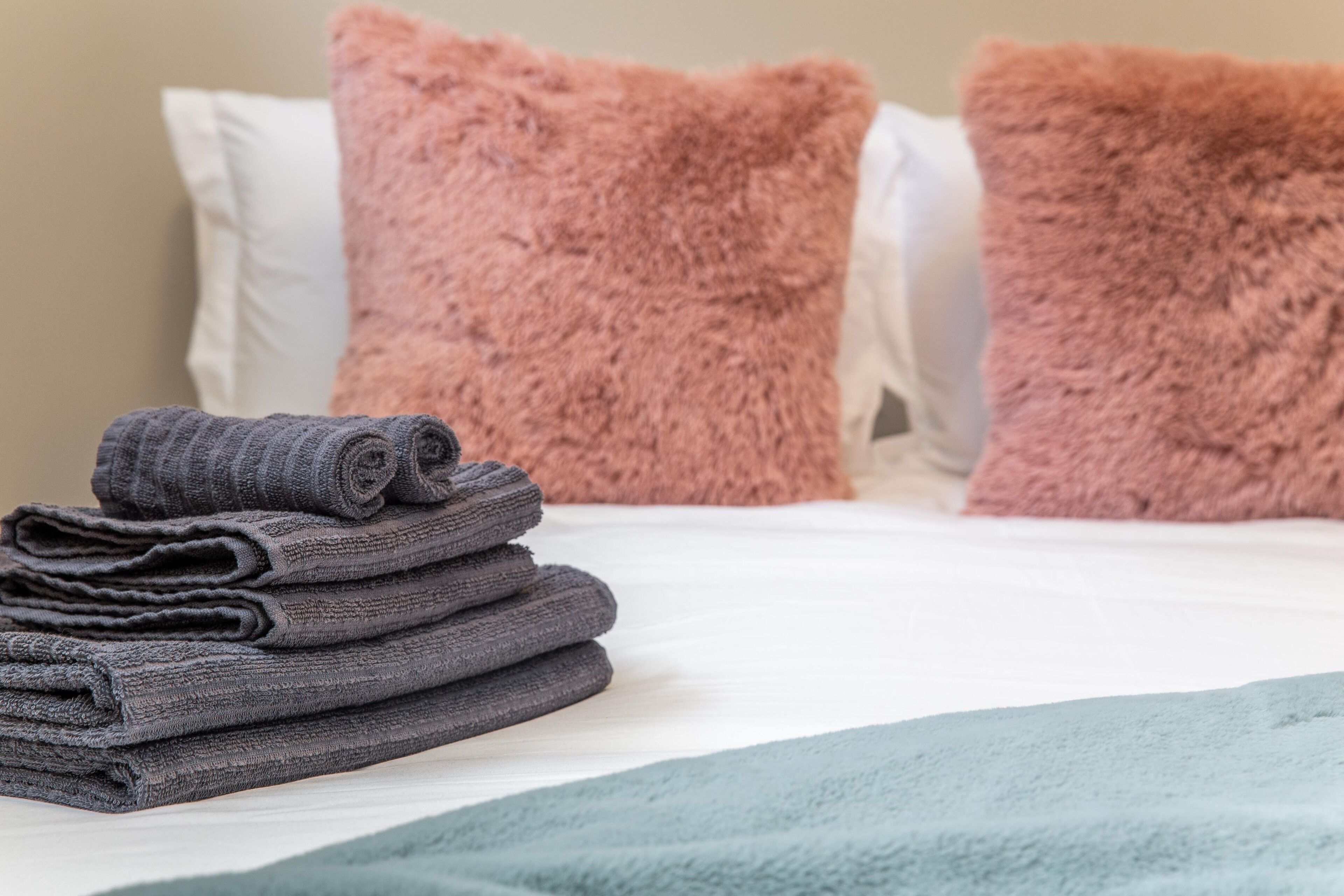Una cama bien hecha con una toalla gris doblada y dos almohadas mullidas.