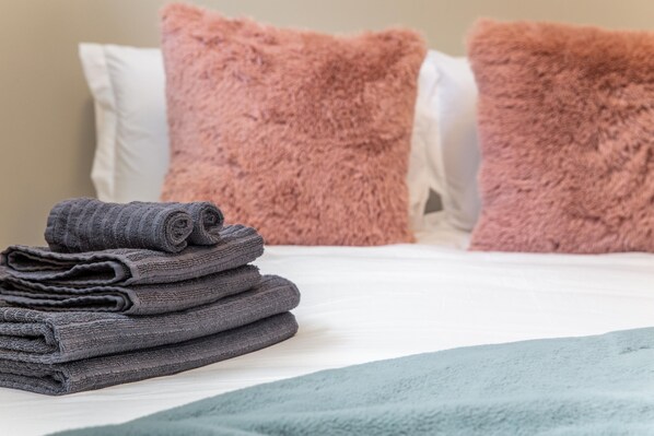 A neatly made bed with a folded gray towel and two fluffy pillows.