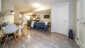 A modern living room with a sofa, chairs, and a dining table. There is a kitchen area in the background with cabinets and a microwave. - ★Bright Modern Suite ★ Netflix - WiFi ✔Long Stays ★ Clean (Edmonton)