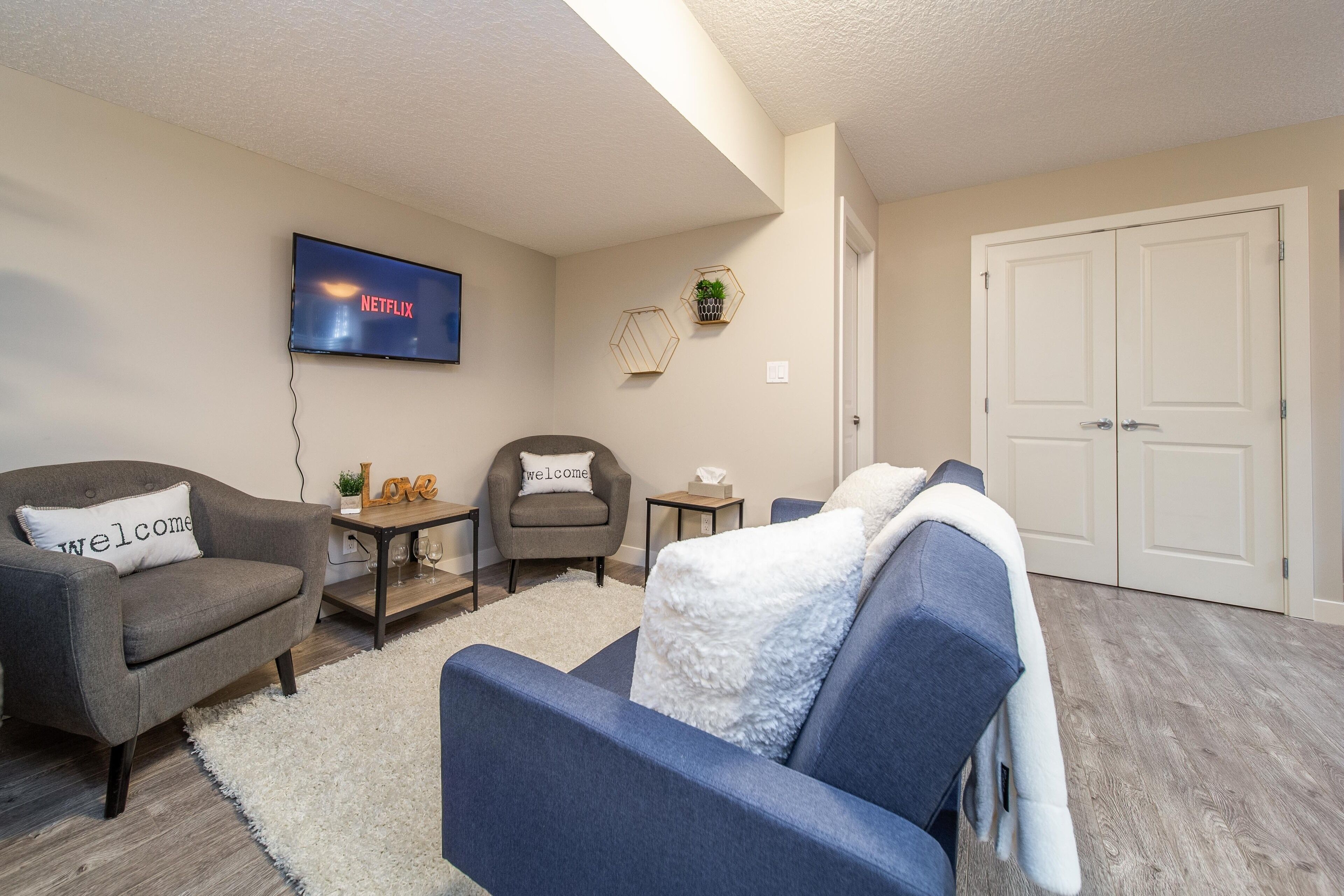 A living room with a flat-screen TV, a sofa, a chair, a small table, and a door.