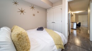 A bedroom with a bed, white walls, and star decorations. There is a hallway leading to a kitchen area. - ★Bright Modern Suite ★ Netflix - WiFi ✔Long Stays ★ Clean (Edmonton)