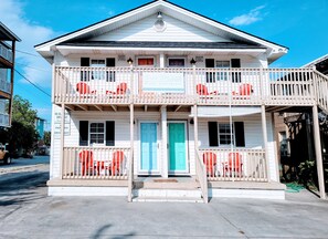 Un immeuble de deux étages avec un balcon à chaque niveau, une porte bleue et une enseigne indiquant qu’il s’agit d’un appartement situé en bord de mer.