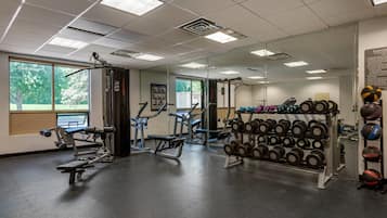 A gym with various exercise equipment, including dumbbells and weight machines, and large windows providing natural light.
