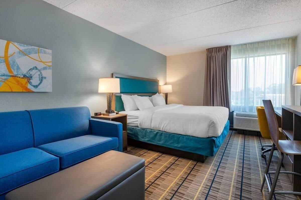 A hotel room with a bed, a blue sofa, a desk, and a window with curtains.