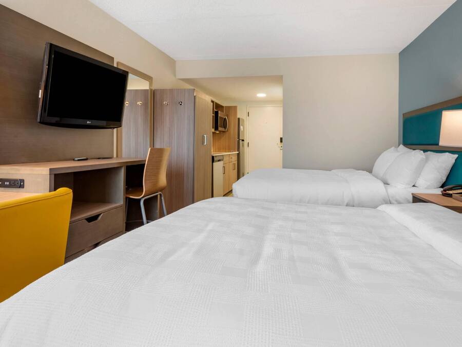A hotel room with a bed, a desk with a chair, a television, and a lamp.