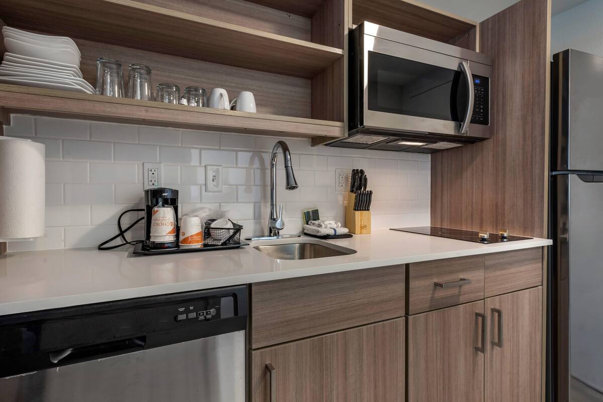 A modern kitchen with a stainless steel dishwasher, a built-in microwave, and wooden cabinets.