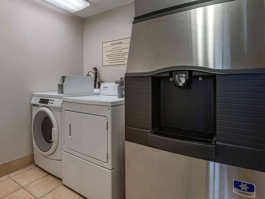 Een kleine wasruimte met een voorlader wasmachine en droger, een waterfontein en een bordje dat gastenwasserijservices aangeeft.