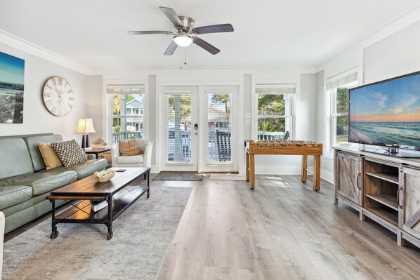 A spacious living room with a green sofa, a coffee table, a foosball table, and a television.