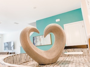 Unique heart-shaped sculpture sits atop a circular bench in a stylish room with a geometric-patterned floor.