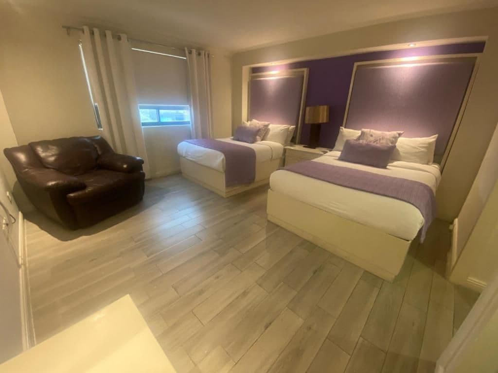 A hotel room with two beds, a leather chair, and a large window.