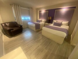 A hotel room with two beds, a leather chair, and a large window.