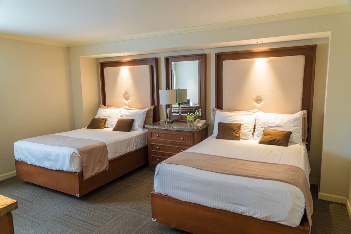 Une chambre d’hôtel avec deux lits simples, une commode en bois, un miroir et une lampe.