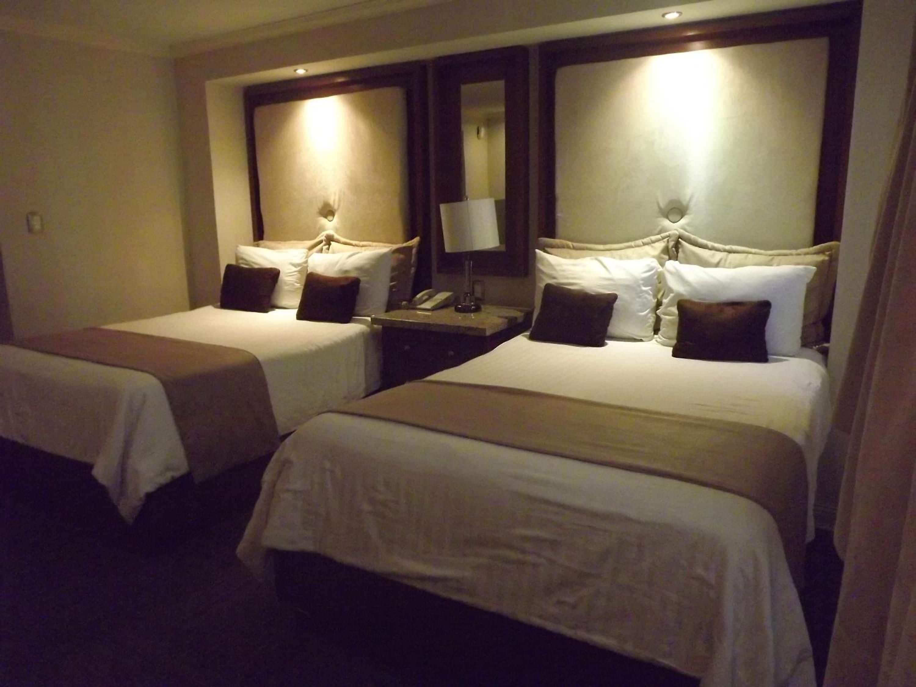 A hotel room with two beds, each with a headboard, bedside tables, and lamps.