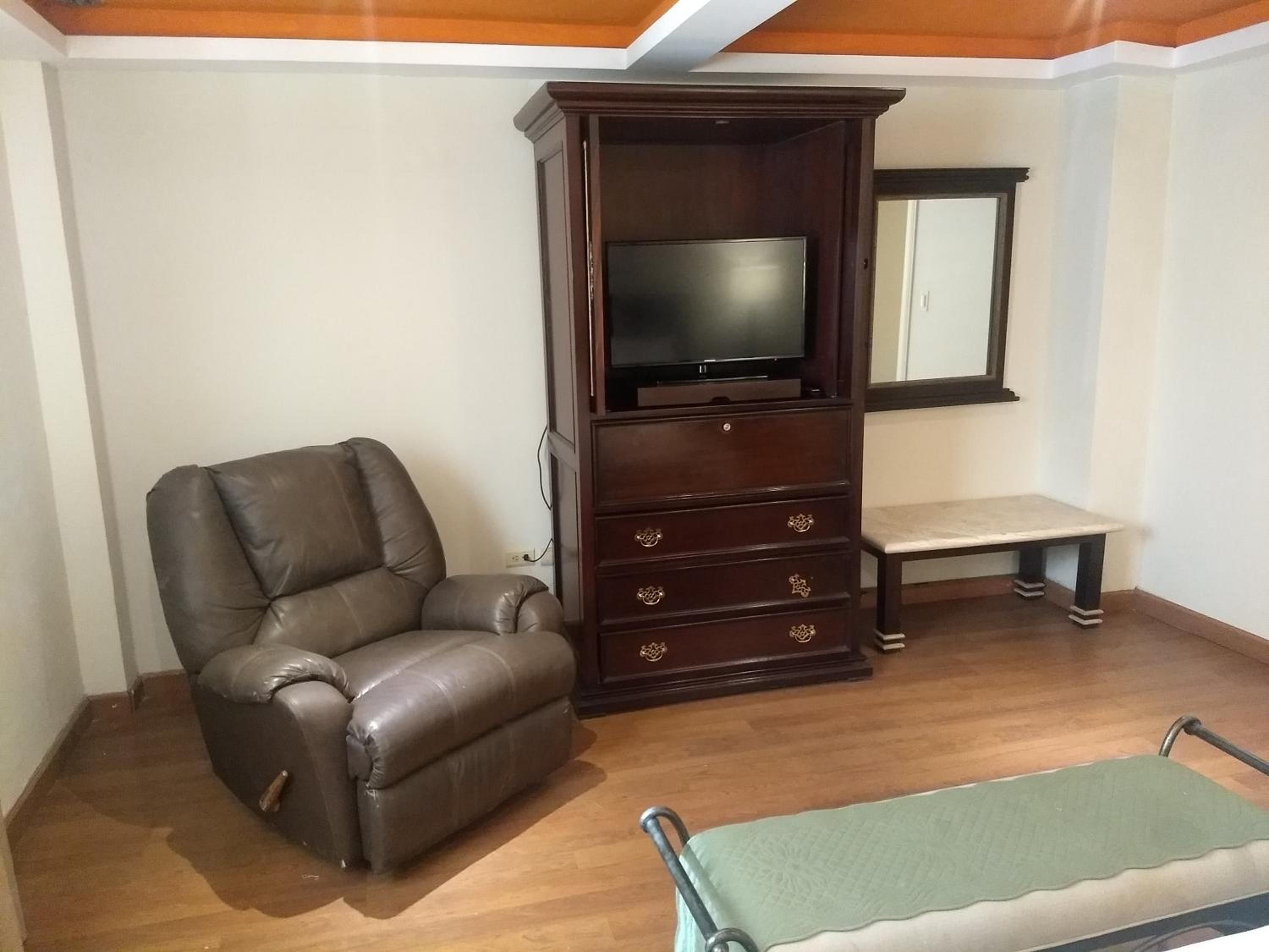 A living room with a leather armchair, a wooden entertainment unit with a television, and a bench.