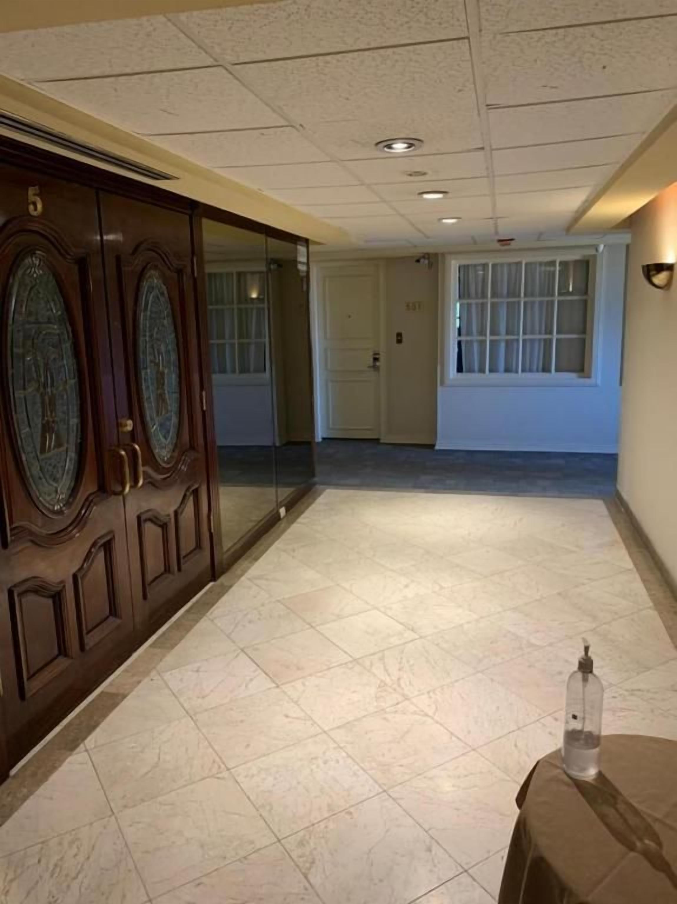 A hallway with a wooden door, a glass door, and a tiled floor.