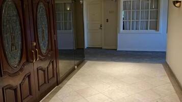 A hallway with a wooden door, a glass door, and a tiled floor.