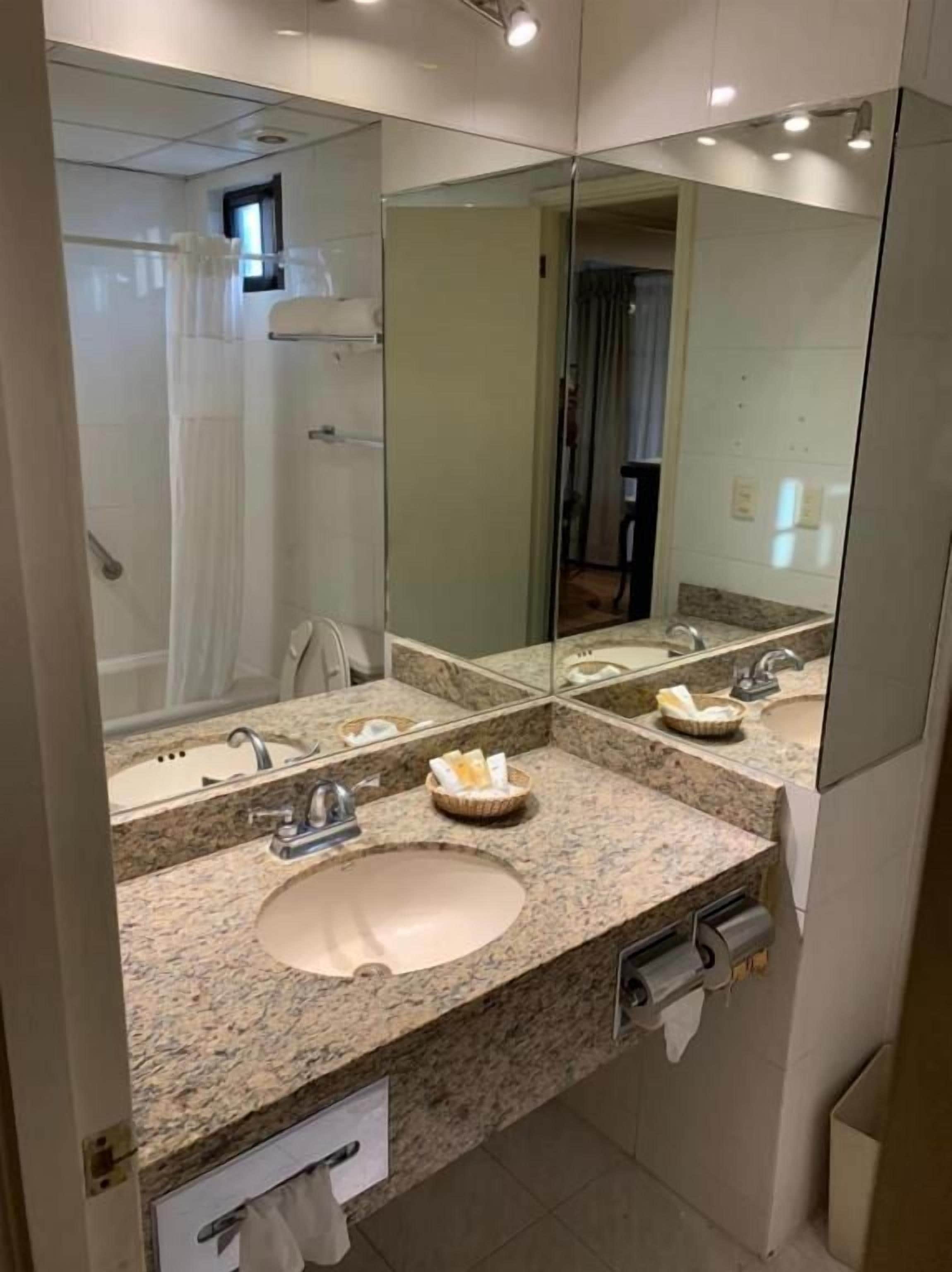 A bathroom with a granite countertop sink, a mirror, and a shower area.